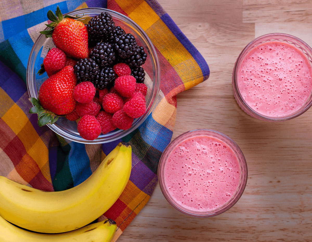 Two servings of a berry berry smoothie with a bowl of mixed berries