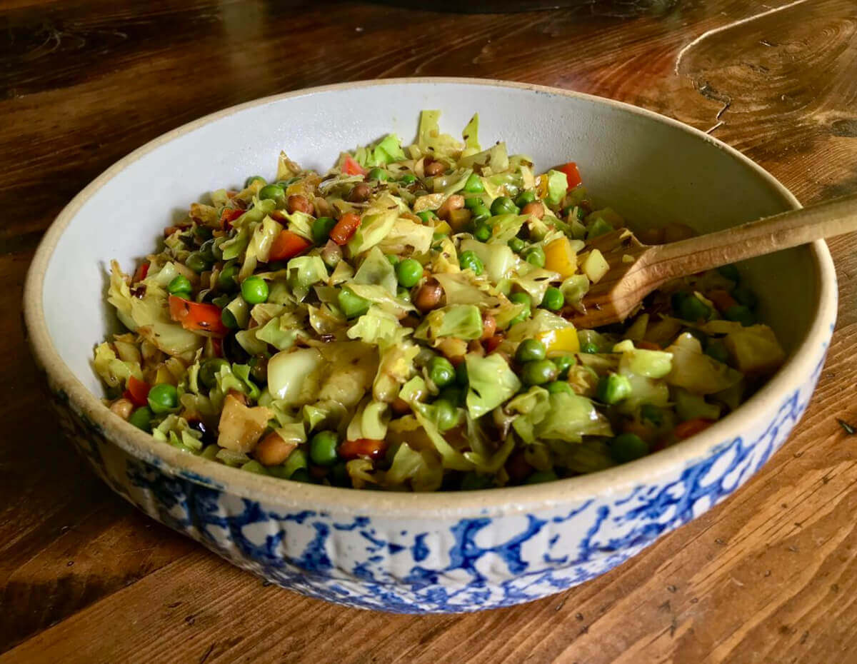 A bowl of stir-fried cabbage with red peppers peanuts and peas