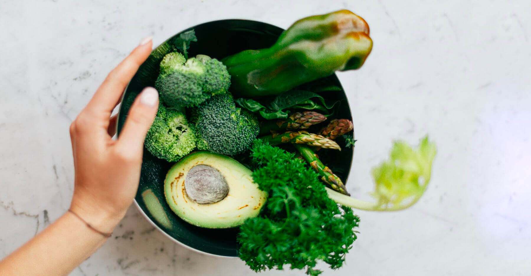 A bowl of fresh vegetables like avocado and broccoli