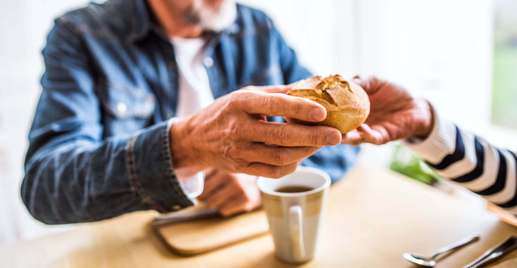 A man handing a dinner roll to another person