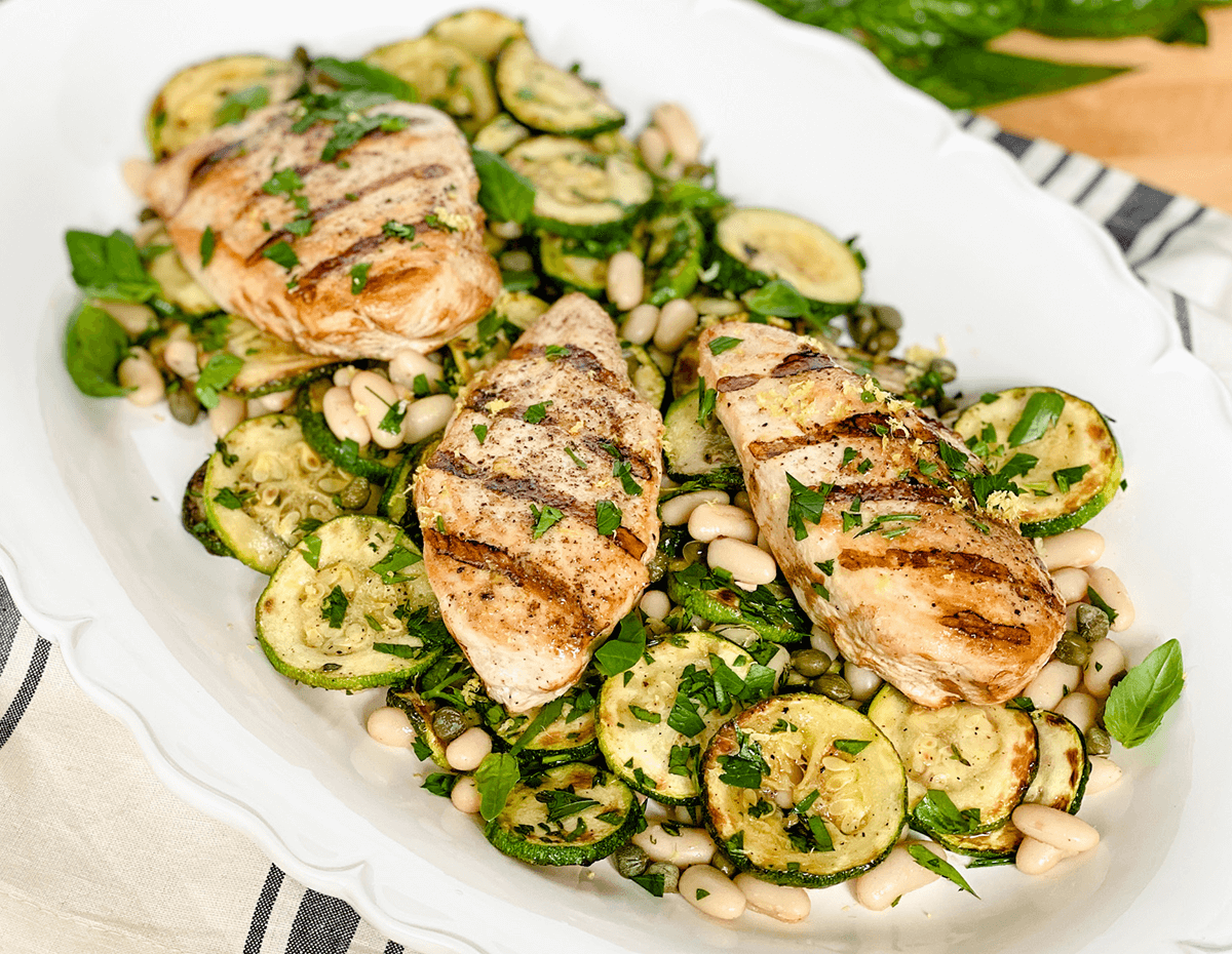 Grilled pesto chicken with braised zucchini and fresh time served on a platter