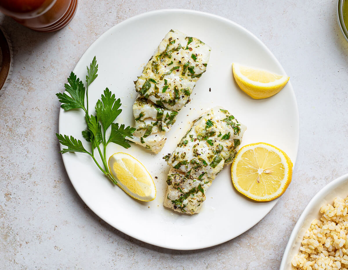 Two fillets of roasted haddock served with lemons and topped with cilantro
