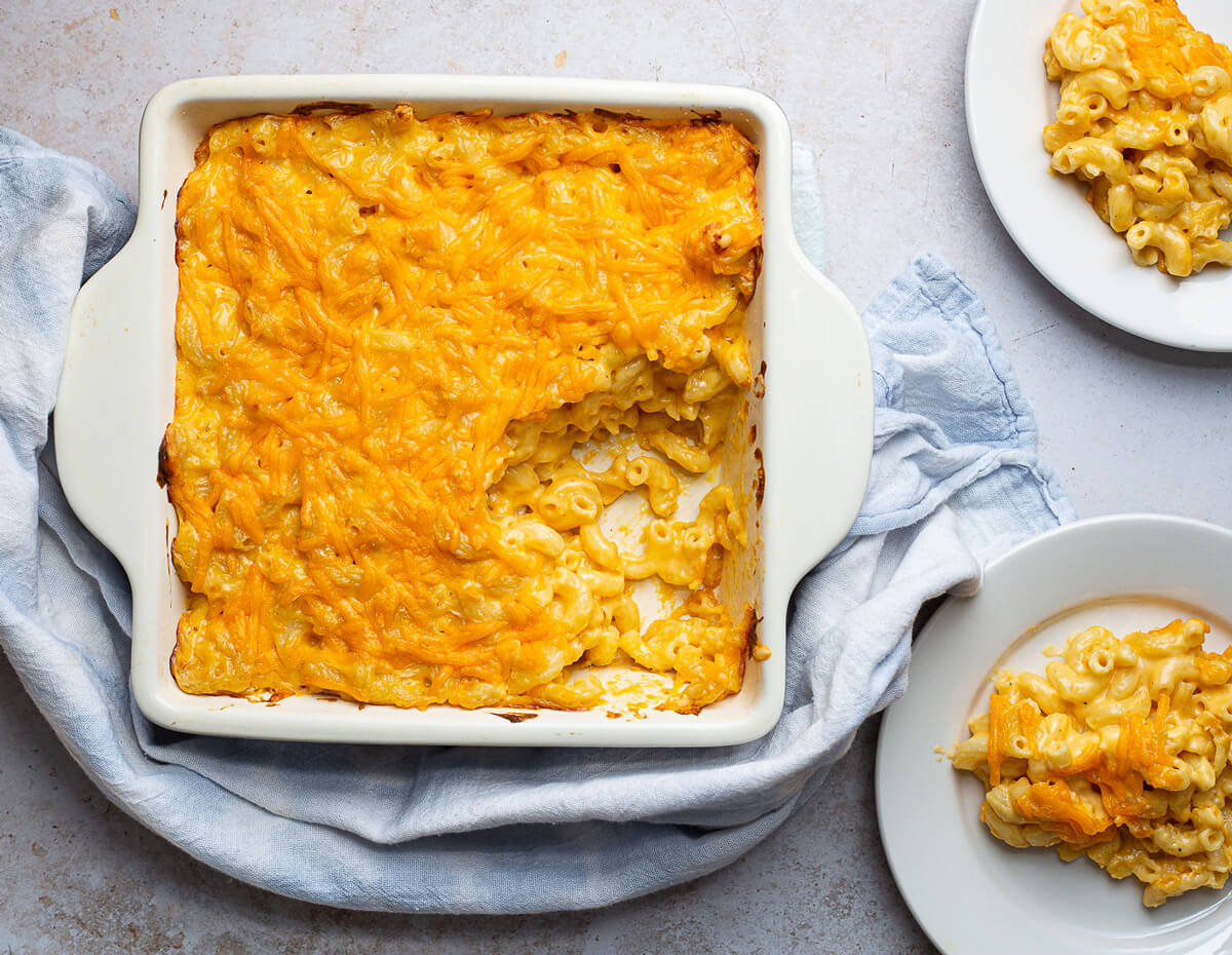 A casserole dish and two servings of freshly baked super cheesy mac n' cheese